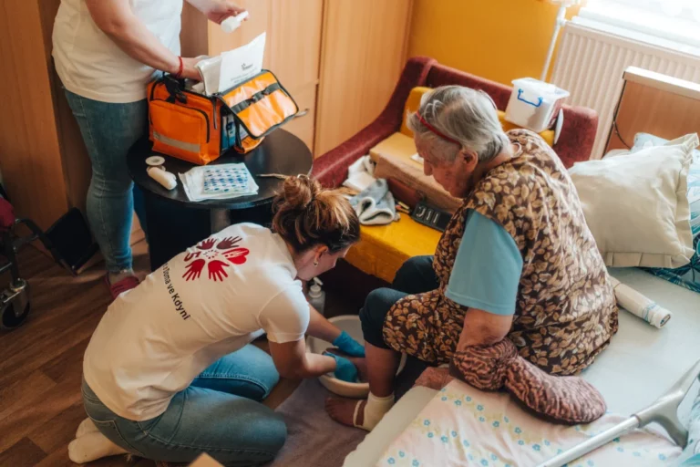 Zdravotn&iacute; sestřička Doma ve Kdyni sed&iacute; v křesle a připravuje zdravotnick&eacute; pomůcky, fotografie je vložen&aacute; do tvaru d&iacute;lku puzzle.